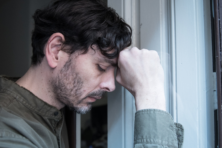 Lonely young man looking outside house balcony looking depressed, destroyed, sad and suffering emotional crisis and grief thinking of taking a difficult and important life decisionの写真素材