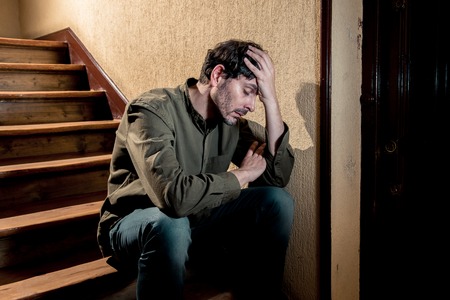 depressed latin man sitting head in hands inside in a stairwell feeling lonely and sad and stressed about work and life in a mental health conceptの写真素材