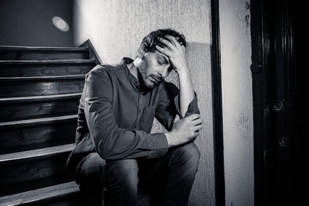 depressed latin man sitting head in hands inside in a stairwell feeling lonely and sad and stressed about work and life in a mental health conceptの写真素材