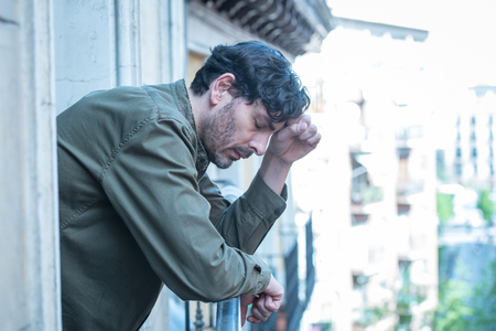 close up portrait of sad and depressed man looking out the window on a balcony at home suffering depression and felling lonely in mental health conceptの写真素材