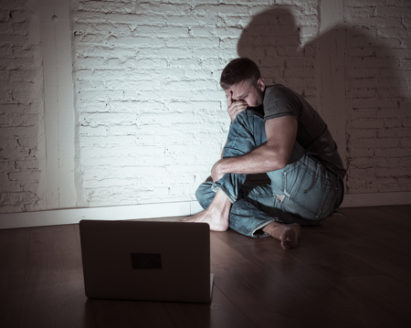 Severely distraught young men with computer laptop suffering cyberbullying and harassment being online abused by stalker or gossip feeling desperate and humiliated in cyber bullying concept.の写真素材
