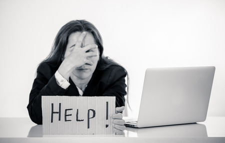 Young attractive latin woman showing help sign desperate suffering stress at work while sitting at office laptop computer desk in business overwork female feeling stressed and overwhelmed.の写真素材