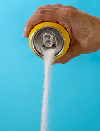 Hand holding soda can pouring lots of sugar in metaphor of sugar content of a refresh drink in healthy nutrition, diet, sweet and carbonated drinks addiction and unhealthy food concept.の写真素材