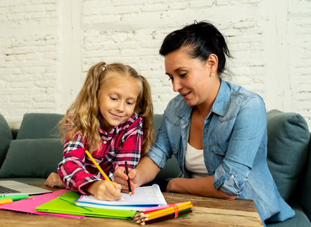 Beautiful mother helping her young blonde cute sweet girl to do homework at home in homework parenting and education concept.の写真素材