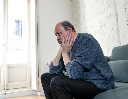 Senior old man feeling desperate sad looking worried depressed thoughtful and lonely on couch at home in Aging Mental health Personal problems and Life style concept.の写真素材