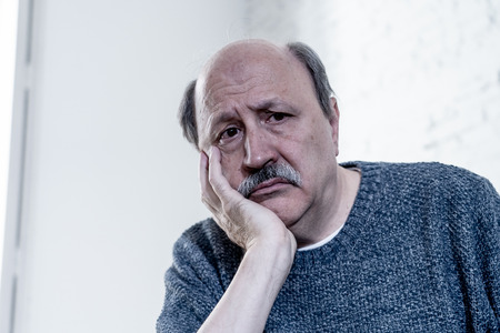 Senior old man feeling desperate sad looking worried depressed thoughtful and lonely on couch at home in Aging Mental health Personal problems and Life style concept.の写真素材