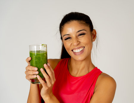 Fitness woman happy smiling holding glass of green vegetable smoothie after fitness running workout isolated on gray background in Beauty Health Fitness Diet Nutrition and healthy Lifestyle concept.の写真素材