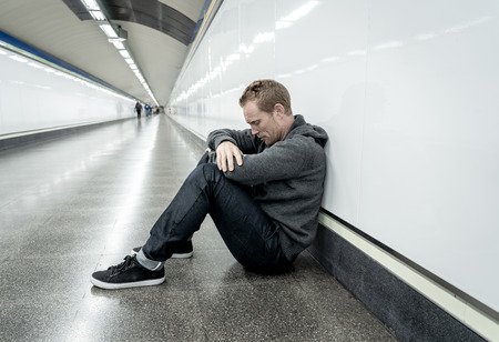 Miserable jobless young man crying Drug addict Homeless in depression stress sitting on ground street subway tunnel looking desperate leaning on wall alone in Mental disorder Emotional pain Sadness.の写真素材