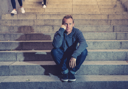 Young desperate jobless man in casual clothes abandoned lost in depression sitting on ground...