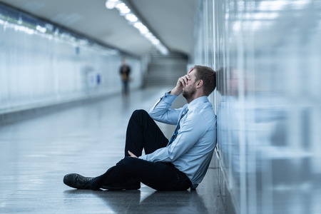 Young jobless business man suffering depression sitting on ground street underground leaning on wall alone looking desperate in Emotional pain Mental health Unemployment and Human emotions concept.の写真素材