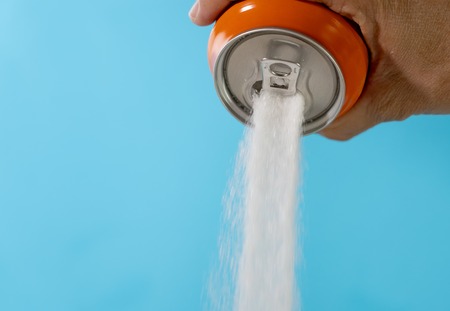 Hand holding soda can pouring crazy amount of sugar in metaphor of sugar content of refreshing drink isolated on red background in Nutrition Diet Unhealthy food Addiction and Excess calories content.の写真素材
