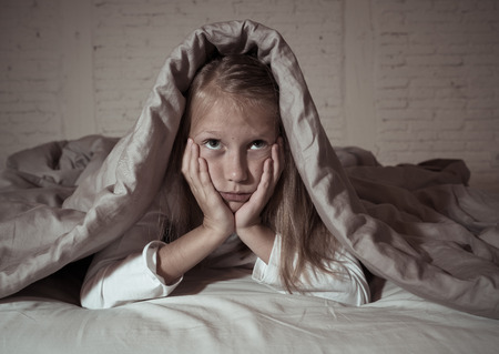 Cute little caucasian girl lying in bed covering her head with blanket feeling exhausted and sleepless suffering from insomnia Depression Stress in Children Emotional and Sleeping Disorders concept.の写真素材