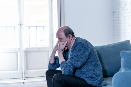 Overwhelmed old senior man suffering alone at home feeling confused sad alone on couch at home in Aging Retirement widower Dementia and Alzheimer concept.の写真素材