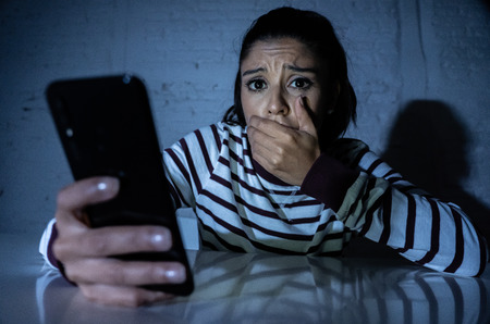 Frightened teenager or young woman using smart mobile cell phone as internet cyberbullying by message stalked abused victim.の写真素材