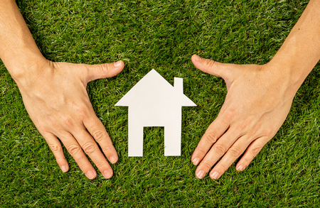 Conceptual picture of woman hands protecting white house on green field top view and copy space in Property investment Real estate Saving and buying a home mortgage insurance and banking concept.の写真素材