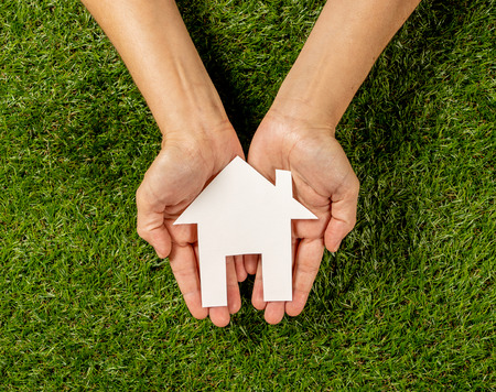 Conceptual picture of woman hands holding white house over green grass field top view and copy space in Property investment Real estate Saving and buying a home mortgage and loan banking concept.の写真素材