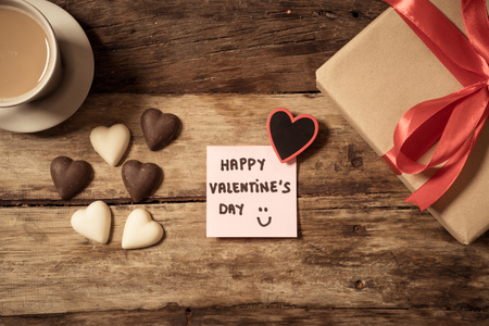 Beautiful top view Valentines composition of gift, chocolate heart shaped, coffee and Happy Valentines day note written on post note in vintage style wooden table background in love celebration concept.の写真素材