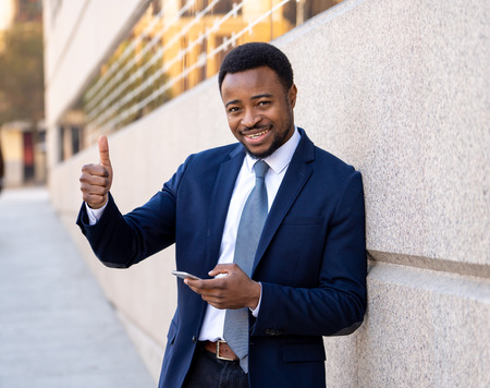 Young man in smart wear on mobile phone sending text email or social media app outdoors at city street. Happy business people, working outside, entrepreneur and work freedom communication technology.の写真素材