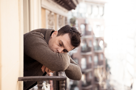 Sad unhappy depressed young man crying and suicidal feeling desperate, isolated and worthless staring down the street on home balcony In People Depression and Mental Health concept. Urban background.の写真素材