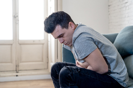 Portrait of young man felling depressed and desperate crying alone in sofa home suffering emotional pain and unhappiness. In People Broken heart, Bullying Depression and Mental health issues concept.の写真素材