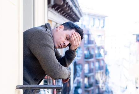 Sad unhappy depressed young man crying and suicidal feeling desperate, isolated and worthless staring down the street on home balcony In People Depression and Mental Health concept. Urban background.の写真素材