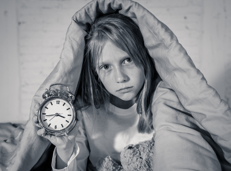 Cute sleepless little girl sitting on bed looking sad and tired having sleeping troubles staying asleep at night or waking too early in the morning in Insomnia Anxiety Sleep Disorders in children.の写真素材
