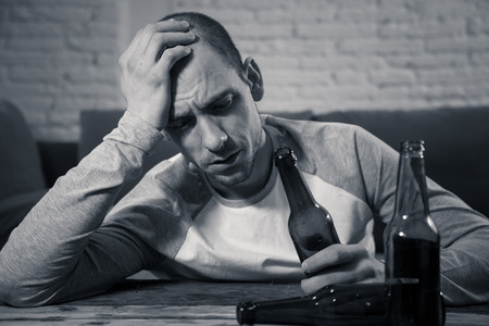 Young sad drunk men drinking beer and alcohol feeling wasted, lonely and desperate in pain and emotional stress. People and Alcohol abuse, addiction and man depression concept. Dramatic lightの写真素材