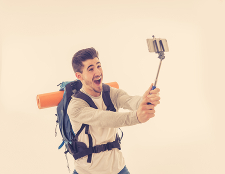 Portrait of young backpacker taking a selfie with his mobile phone isolated on white background. In...