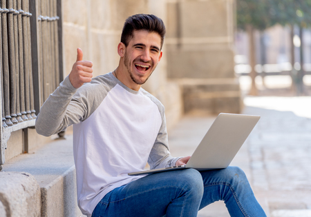 Young attractive trendy man in casual clothes studying working on laptop on the internet, blogging, chatting and checking email on steps in a european city. In Student learning online and lifestyle.の写真素材