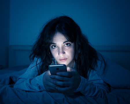 Addicted young woman chatting and surfing on the internet using her smart phone sleepy, bored and...