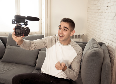 Life style portrait of young happy male blogger on camera screen filming a video tutorial for the internet. Millennial people, new fashion and modern technology, freelance and creative work concept.の写真素材
