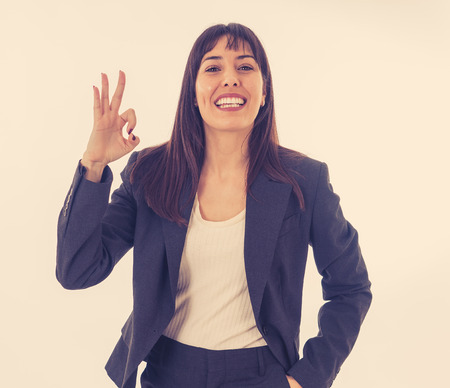 Half length portrait of young pretty business woman standing and making all OK gesture. Smiling feeling confident and successful. In people business education, success and work environment concept.の写真素材