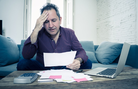 Mature attractive man on computer looking stressed and worried with credit card payments and home finances accounting costs charges taxes and mortgage in paying bills financial problems and debts.の写真素材