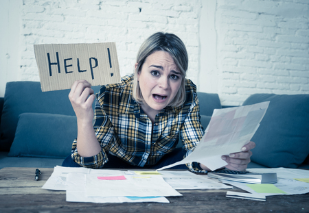 Lifestyle portrait of worried desperate young woman feeling stressed while working through finances at home showing Help sign. In single mother paying off debts and bills and financial problems.の写真素材