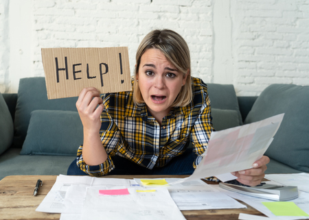 Lifestyle portrait of worried desperate young woman feeling stressed while working through finances at home showing Help sign. In single mother paying off debts and bills and financial problems.の写真素材
