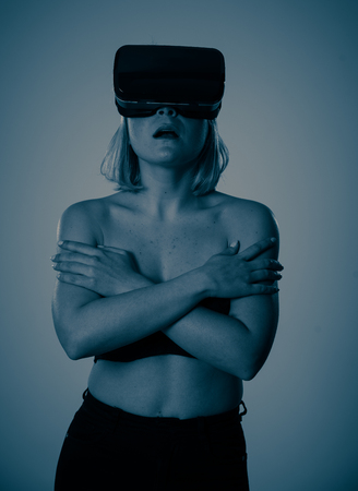 Sensual attractive woman using augmented or virtual reality goggles feeling excited exploring virtual sexuality while getting topless covering her breast. In cyber sex VR simulator and new technology.の写真素材