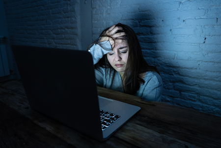 Dramatic portrait of sad scared young woman stressed and worried staring at laptop suffering cyber bullying and harassment. Victim of online abuse and intimidation by stalker. In dangers of internet.の写真素材