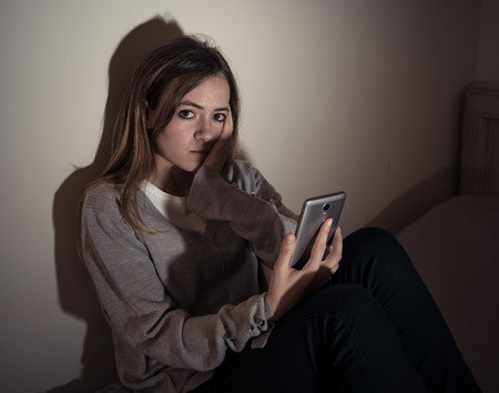 Young teenager girl suffering mobile cell phone addiction feeling lonely and depressed having insomnia needing to be connected sitting on bed late at night. Inの写真素材