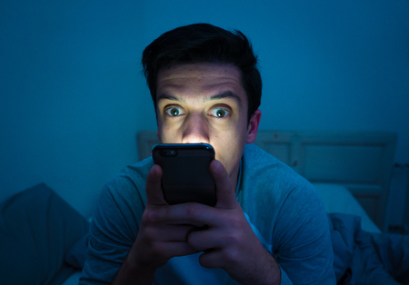 Young mobile phone addict man awake at night in bed using smartphone for chatting, flirting and sending text message. In communication, Internet addiction and Social media network abuse conceptの写真素材