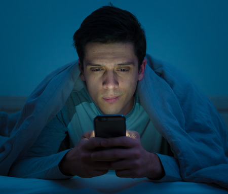 Young mobile phone addict man awake at night in bed using smartphone for chatting, flirting and sending text message. In communication, Internet addiction and Social media network abuse conceptの写真素材