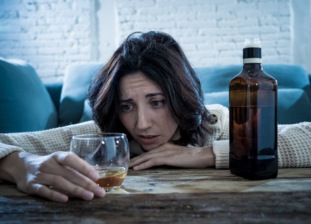Drunk alcoholic depressed woman drinking scotch whiskey spirits alone at home. Feeling hopeless, week and lonely. In People lifestyle, Depression, alcohol addiction, alcoholism and drug abuse concept.の写真素材