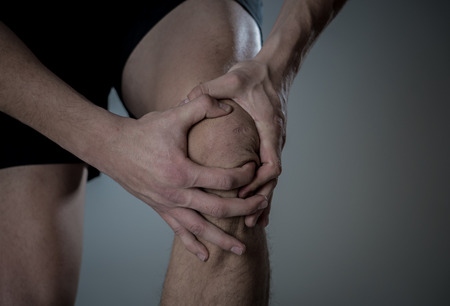 Young fit man holding knee with hands in pain after suffering muscle injury broken bone leg pain sprain or cramp during running workout. In Body pain and sport training injury and body health care.の写真素材