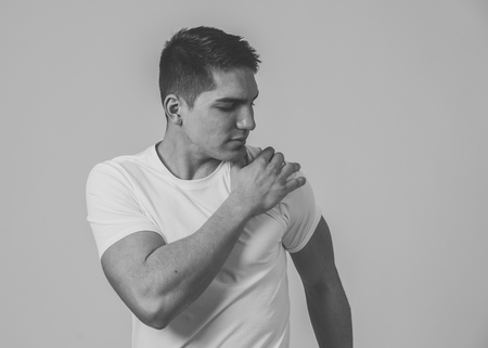Young muscular fitness man touching and grabbing his shoulder suffering strong pain. Isolated on neutral background. In sport injury Incorrect posture problems and body health care.の写真素材
