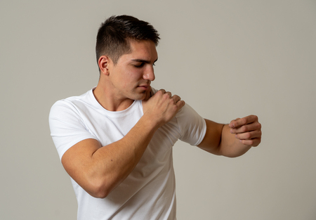 Young muscular fitness man touching and grabbing his shoulder suffering strong pain. Isolated on neutral background. In sport injury Incorrect posture problems and body health care.