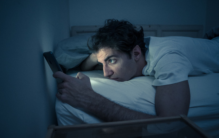 Addicted to social media young man chatting and surfing on the Internet on smart phone at night in...