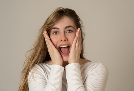 Beautiful young blonde teenager woman with happy face making surprised gestures looking and pointing at something shocking and good. Human facial expressions and emotions. Portrait with copy space.の写真素材
