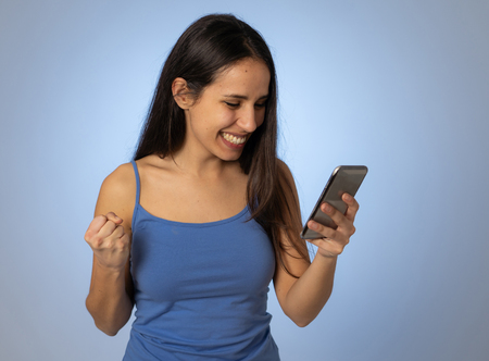 Young latin woman on mobile looking happily shocked at social media app dating site. Teenager girl having lots of followers and likes on online video blog In millennial generation using technology.の写真素材