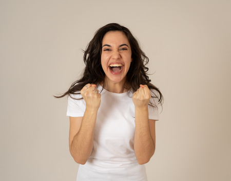 Young attractive latin woman celebrating success winning or feeling lucky and joyful dancing making celebration gestures with arms. Isolated on neutral background In People expressions and emotions.の写真素材