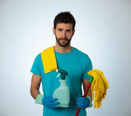 Young attractive man tired and upset holding bucket mop and cleaning spray feeling sad frustrated and lazy in domestic duties concept and men and women gender roles. Isolated on blue backgroundの写真素材