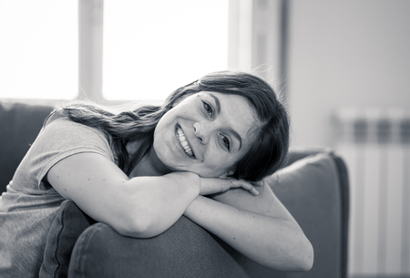 Woman relaxing time. Lifestyle black and white close up portrait of attractive young female with beautiful smile sitting on sofa at home with natural light. In People Well being and leisure concept.の写真素材